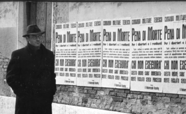 Cette affiche en noir et blanc capte un moment de tension suspendue : un homme seul marche dans une rue déserte de Venise, le regard caché derrière ses lunettes. Sur le mur, une série d’affiches du commandement militaire allemand proclame la "Peine de mort" pour les déserteurs.